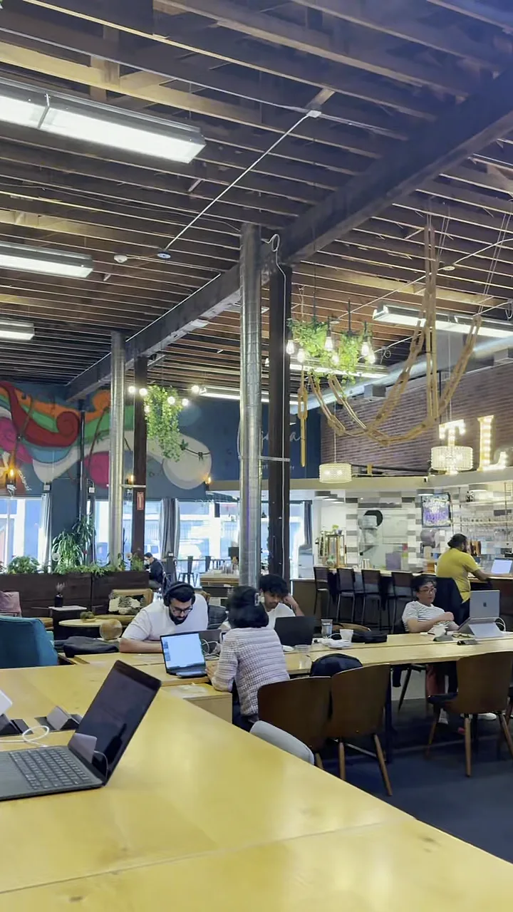 people working on laptops at long tables in trellis san francisco, colorful mural and bar visible in background