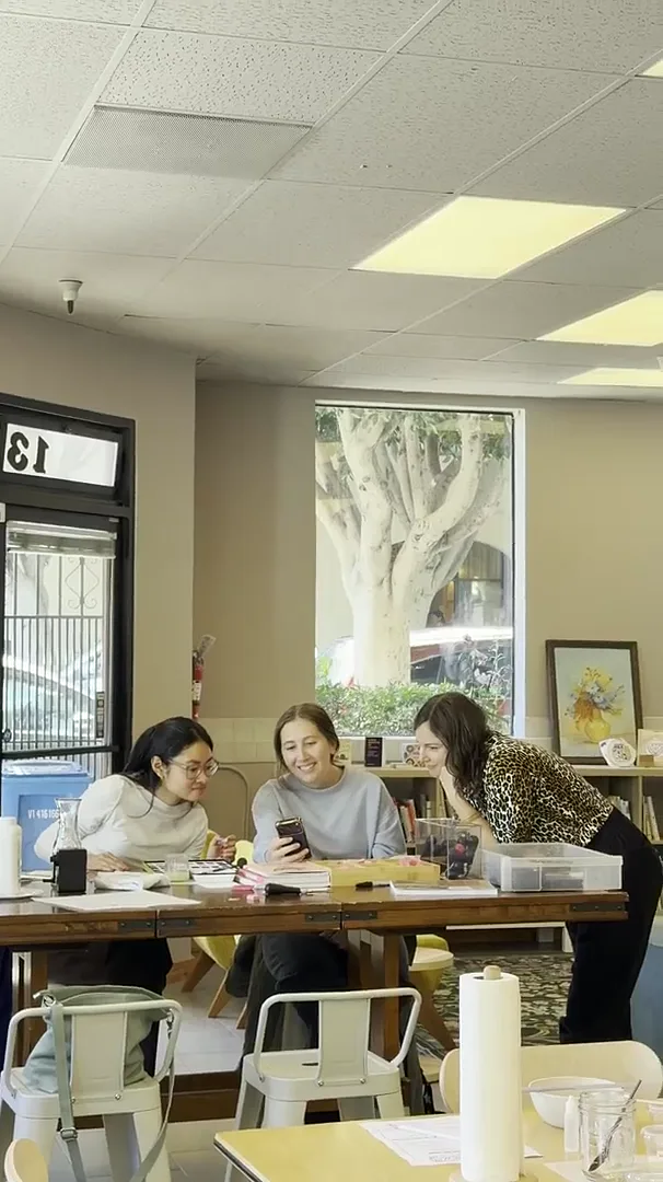 three women gathered around a worktable at society of thumbs, san francisco, with a tree-filled window behind them